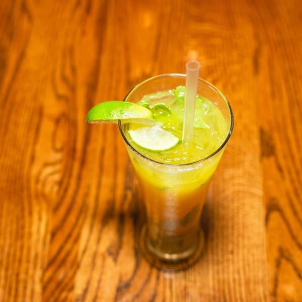 A refreshing Venezuelan cocktail with lime slices and a straw on a wooden table.