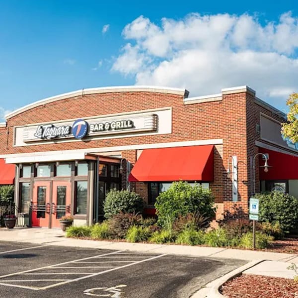 Exterior of La Taguara Bar & Grill, a brick building with red awnings under a blue sky.