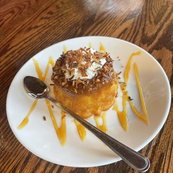 Venezuelan dessert with caramel, whipped cream, and toasted coconut flakes on a white plate with a spoon.