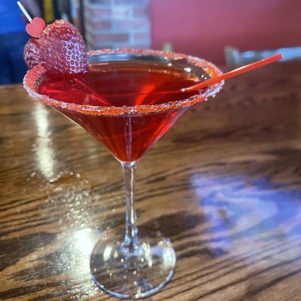 Red martini with a sugar-rimmed glass, garnished with strawberries and a heart pick.
