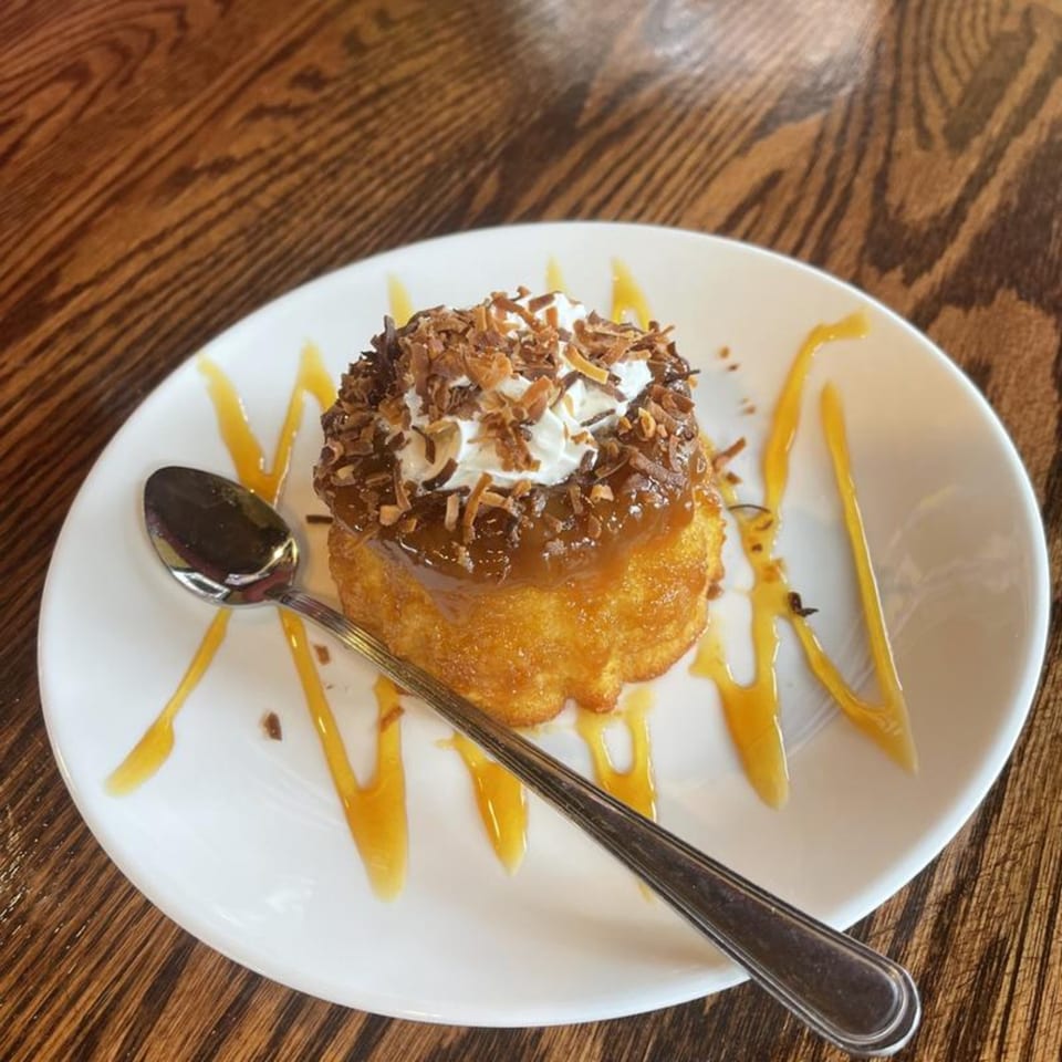 Venezuelan dessert with whipped cream, caramel, and toasted coconut flakes on a white plate with a spoon.