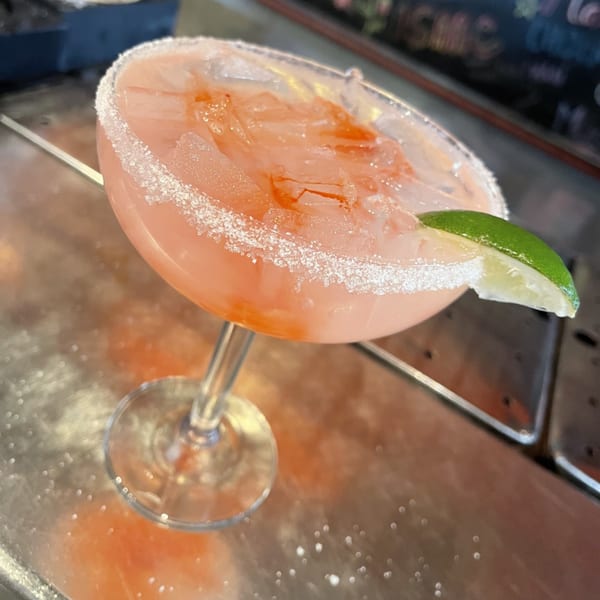 A vibrant pink margarita with a salted rim and lime wedge, on a metallic bar surface.