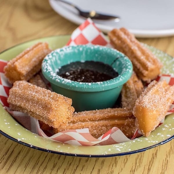 Venezuelan churros with powdered sugar and chocolate dipping sauce in a green bowl.
