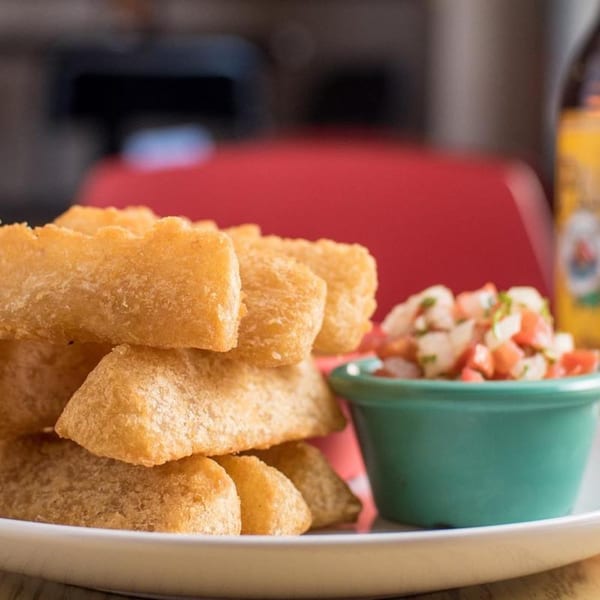 Golden fried yuca sticks piled on a white plate with a side of fresh pico de gallo.