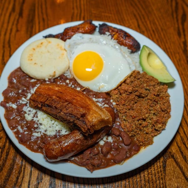 Venezuelan breakfast with beans, rice, fried egg, arepa, avocado, plantains, and meats on a white plate.