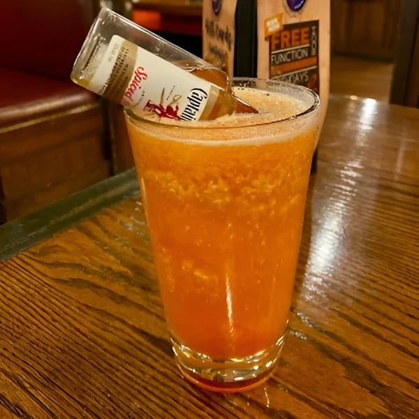 An orange cocktail with a Captain Morgan Spiced Rum bottle inverted into it on a wooden table.